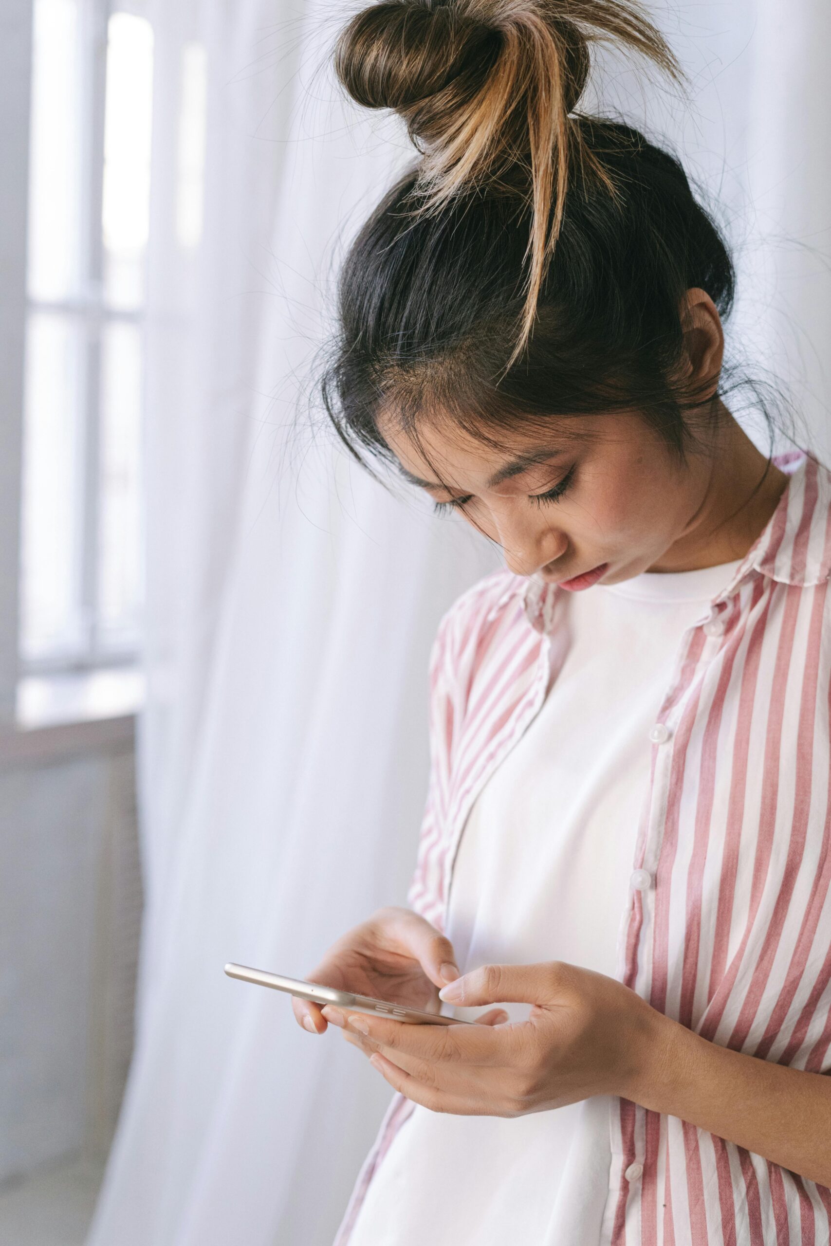Young woman in a striped shirt using a smartphone indoors, focused on the screen.